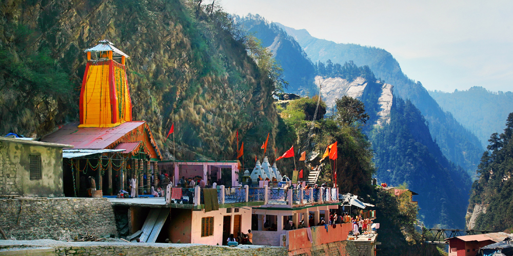 The side view of Char dham Yamunotri site covered with mountains & adorned with divine hinduism flags.